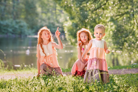 Three red-haired sisters in long linen dresses blow bubbles in the park on a sunny summer day.の写真素材