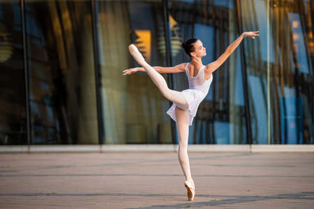 young ballerina in a white leotard dancing on pointe shoes against the backdrop of a cityscapeの写真素材