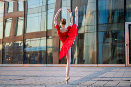 a young ballerina in a bright red tutu is dancing against the backdrop of a cityscapeの写真素材