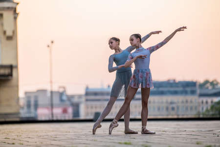 Two young ballerinas dancing in pointe shoes in the city against the backdrop of the sunset skyの写真素材