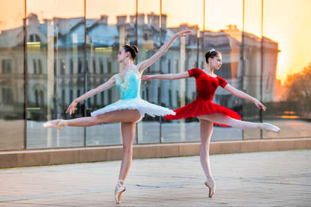 two young ballerinas in a bright red and blue tutu are dancing against the backdrop of the reflection of the city sunsetの写真素材
