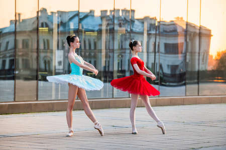 two young ballerinas in a bright red and blue tutu are dancing against the backdrop of the reflection of the city sunsetの写真素材
