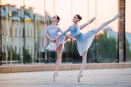 two young ballerinas in pointe shoes are dancing against the background of the reflection of the city sunset in the mirrored wall of the buildingの写真素材