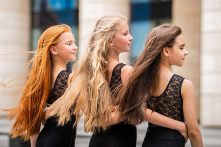 Three teenage girls with loose hair blonde redhead and brunette, stand in profile outside in summer. Vloses develop in the wind.の写真素材