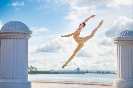 A slender ballerina in pointe shoes and a bridal costume is jumping against the background of the seaの写真素材