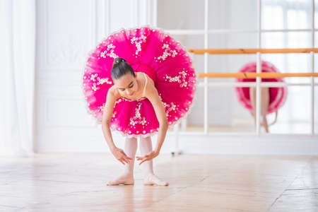 Little ballerina in a bright pink tutu stands in a pose in a beautiful white hallの写真素材