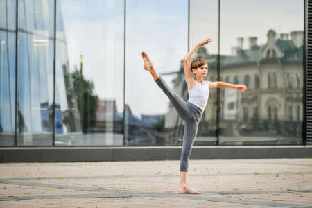 ballet boy teenager dancing against the background of the reflection of the city and the sky in the glass wallの写真素材