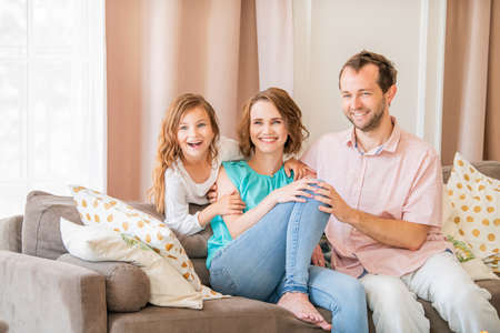 Happy family, mom dad and daughter are sitting on the couch and laughing togetherの写真素材