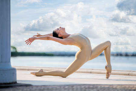 A slender ballerina in pointe shoes and a tight-fitting suit posing against the backdrop of the sea and sky with cloudsの写真素材
