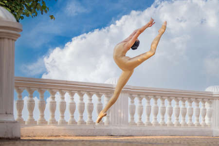 A slender ballerina in pointe shoes and a bridal costume is jumping against the background of the seaの写真素材