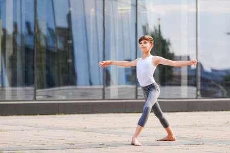 ballet boy teenager dancing against the background of the reflection of the city and the sky in the glass wallの写真素材