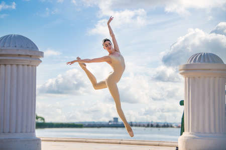 A slender ballerina in pointe shoes and a bridal costume is jumping against the background of the seaの写真素材
