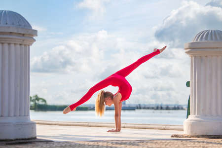 Gymnast teenage girl in a red suit posing on the embankment against the background of the sea and skyの写真素材