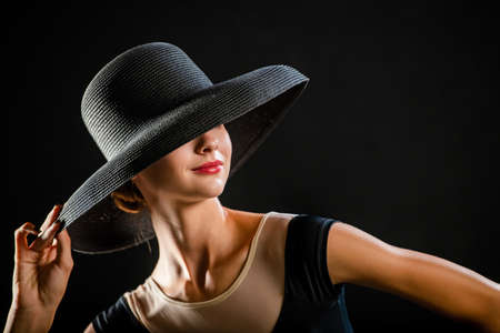 Glamorous portrait of a beautiful sexy young woman on a black background wearing a hatの写真素材