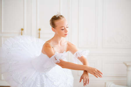 Portrait of a young slender ballerina in a white tutu in an elegant pose in a large beautiful white hall.の写真素材
