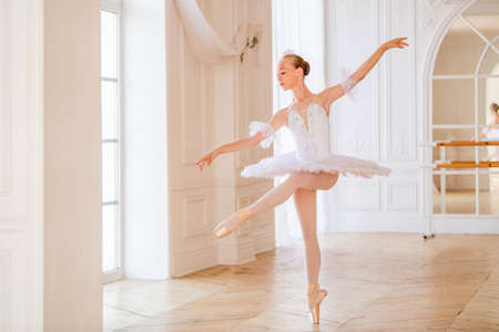 young slender ballerina in a white tutu in pointe shoes is dancing in a large beautiful white hall.の写真素材