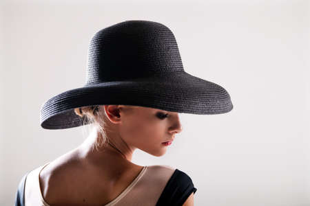 Romantic portrait of a beautiful young girl on a light background in an elegant hatの写真素材
