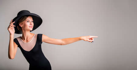 Romantic portrait of a beautiful young girl on a light background in an elegant hat pointing to the...
