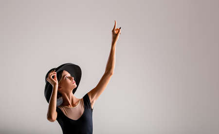 Romantic portrait of a beautiful young girl on a light background in an elegant hat pointing to the rightの写真素材