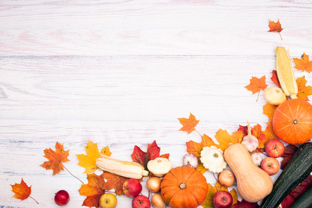 Corner layout with pumpkin, corn, other vegetables and autumn leaves. Top view on a light wooden...