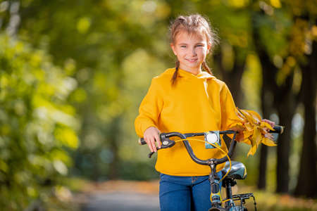 Portrait of a smiling girl in a yellow sweatshirt with a bicycle in an autumn park.の写真素材