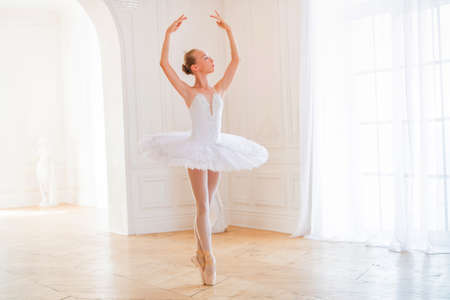 young slender ballerina in a white tutu in pointe shoes is dancing in a large beautiful white hall.の写真素材