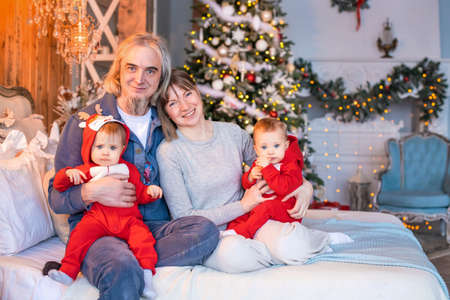 twins toddlers in red reindeer santa claus costumes sit at home with mom and dad on the background...