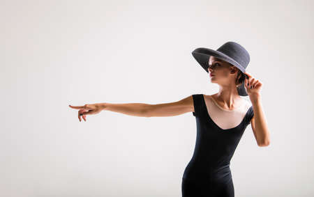 Romantic portrait of a beautiful young girl on a light background in an elegant hat pointing to the...