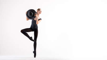 young ballerina in black pointe shoes and black bondage costume posing on a white background with a hat in handの写真素材