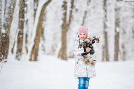 little girl carries a cat in her arms in a snowy winterの写真素材