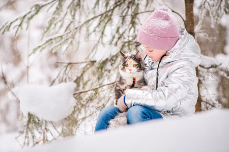 little girl sits with cat in an embrace in the snow in the winter forestの写真素材