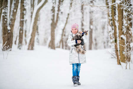 little girl carries a cat in her arms in a snowy winterの写真素材