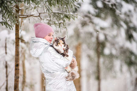 little girl carries a cat in her arms in a snowy winterの写真素材