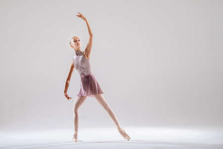 Beautiful young girl ballerina in pointe shoes and a pink swimsuit on a light background.の写真素材