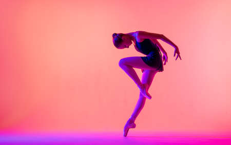 Beautiful young girl ballerina in pointe shoes and swimsuit silhouette on bright red background.の写真素材