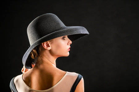 Portrait of beautiful young girl in elegant black hat on black backgroundの写真素材
