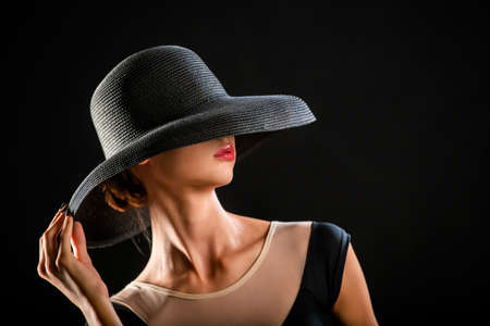 Portrait of beautiful young girl in elegant black hat on black backgroundの写真素材