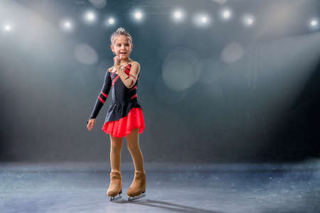 Little skater rides on rings in a red and black dress on the ice arenaの写真素材