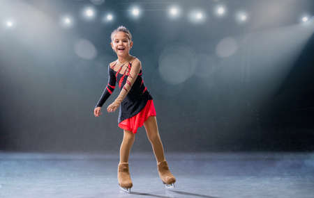 Little skater rides on rings in a red and black dress on the ice arenaの写真素材