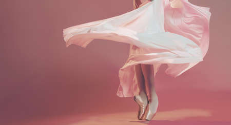 Legs of ballerina in pointe shoes surrounded by flowing skirt stand on beige backgroundの写真素材