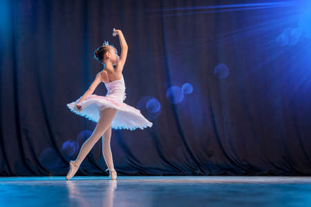 A little girl ballerina is dancing on stage in a white tutu on pointe shoes a classic variation.の写真素材