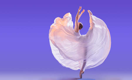 elegant ballerina in pointe shoes is dancing in a long flying white skirt on a lilac light backgroundの写真素材