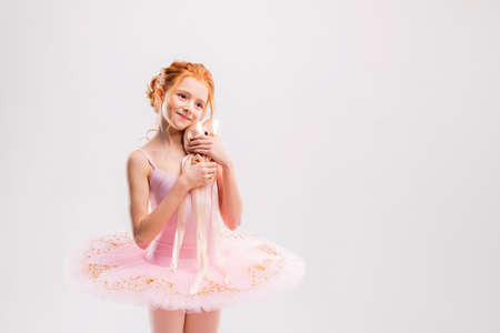 Portrait of little tender red-haired girl in pink tutu with pointe shoes, dreaming of becoming ballerinaの写真素材