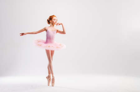 Little ballerina dancer in a pink tutu academy student posing on white backgroundの写真素材