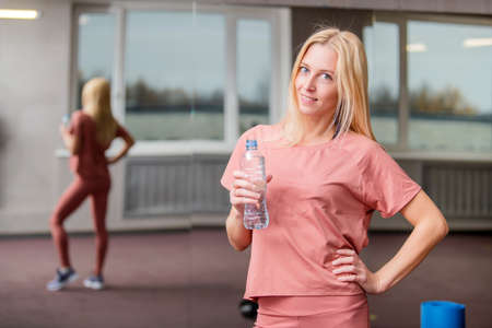 Smiling blonde girl holds a bottle of water in her hand in gym.の写真素材