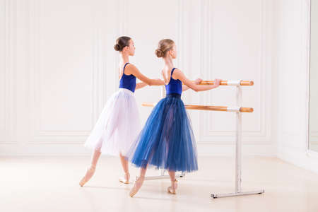 group of two student ballerinas is engaged in pointe shoes at barre in beautiful white room against the backdrop of mirror.の写真素材