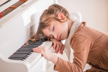 little girl fell asleep on the keyboard on a large white piano in bright sunny roomの写真素材