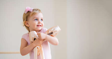 Portrait of cute blue-eyed baby ballerina in pink hugging pointe shoes.の写真素材