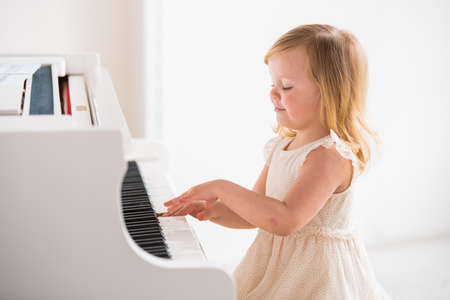 little girl baby plays a big white piano in a bright sunny roomの写真素材