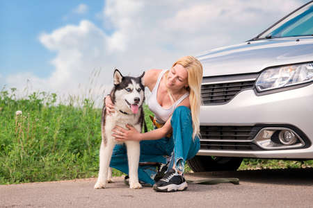 loving hostess hugs her beloved pet Siberian Husky in background of the car in which they travel.の写真素材